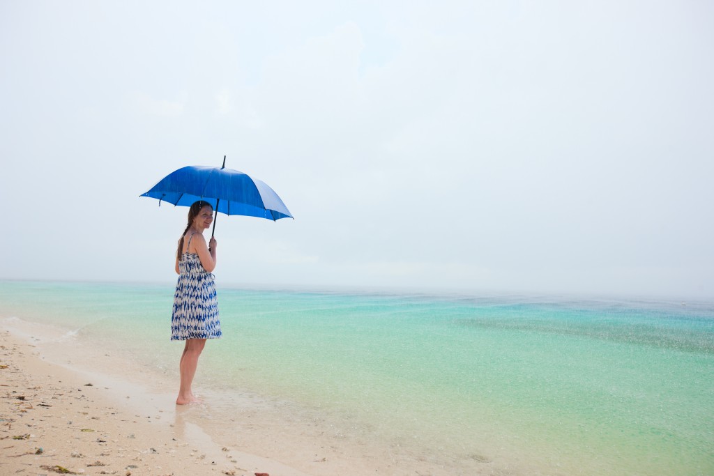 Young woman with blue umbrella staying at beach under the rain