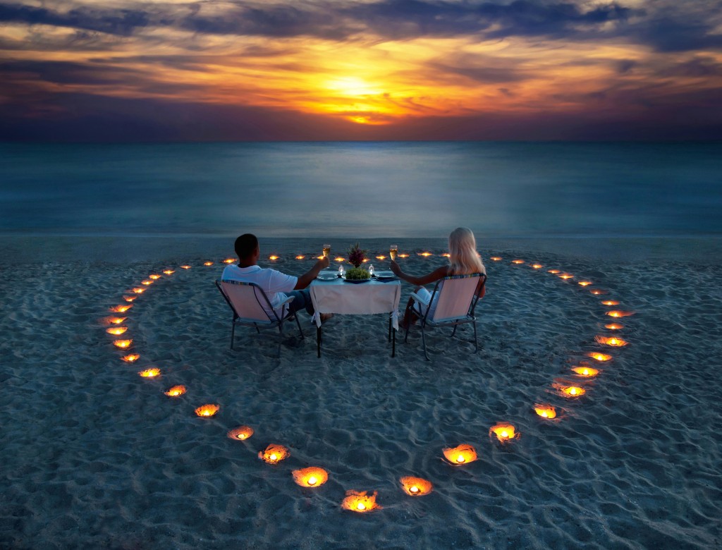 A young couple share a romantic dinner with candles heart on the sea sand beach. Honeymoon in Barbados