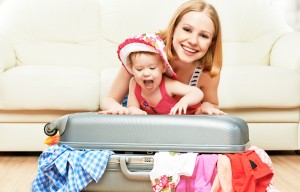Mother and baby girl with suitcase baggage and clothes ready for traveling on vacation. Baby Caribbean Traveling Tips