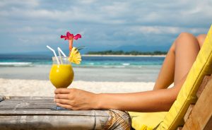 Woman holding a fruit cocktail on a tropical beach. Best Vacation deals