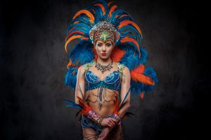 Studio portrait of a woman in a colorful sumptuous carnival feather suit, posing on a dark background. Caribbean carnivals