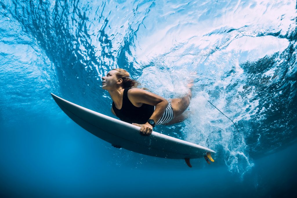 Surfer woman dive underwater. Surfgirl dive under big wave. Surfing in the Caribbean