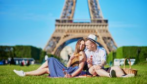 Romantic couple having picnic on grass with wine and fruits near the Eiffel tower in Paris. Honeymoon in France