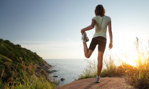Runner stretching on top of a hill and enjoying sunset sea view. Fitness during a holiday