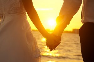 Young adult male groom and female bride holding hands on beach at sunset. best honeymoon destinations.