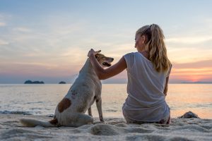 Young woman with dog sitting on the beach. Dog-friendly vacations