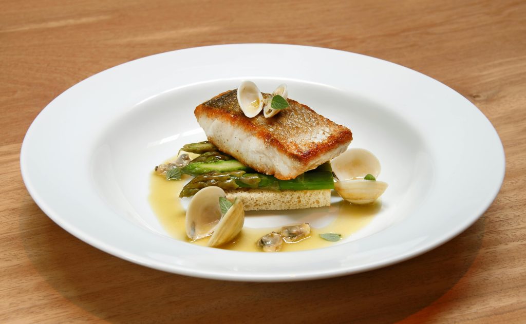 Seared fish with clams and asparagus on a minimalist plate, fine cuisine served at top 10 restaurants in St Barts.