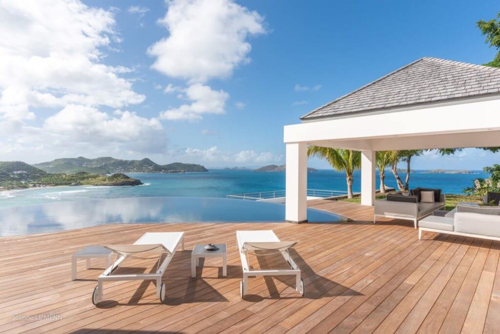 Chic oceanview villa terrace in St Barts with infinity pool and luxury lounge area under clear blue skies.