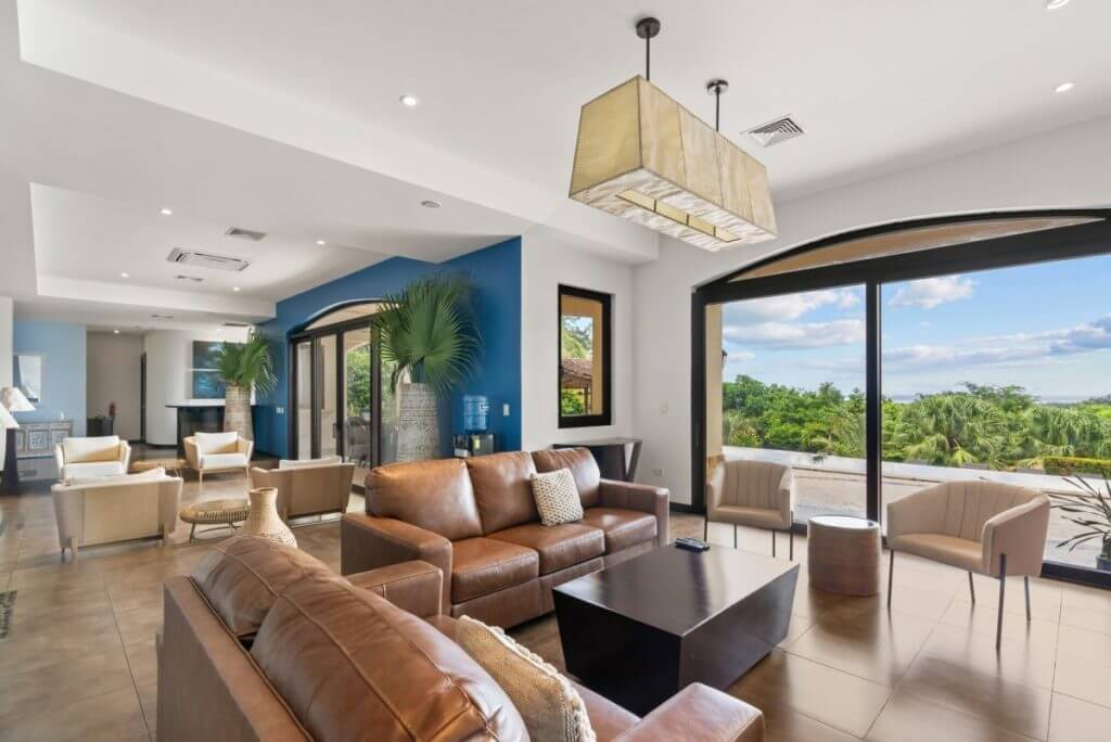 Villa Buena Onda, Costa Rica living room with leather sofas, armchairs, and wide windows framing tropical greenery.