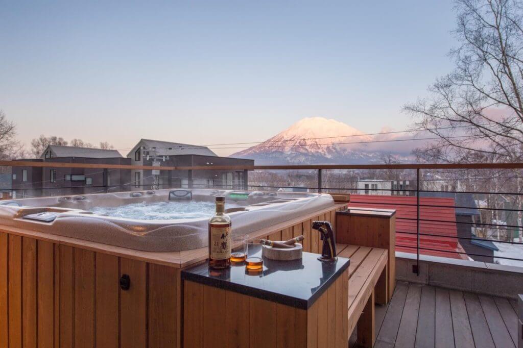 Chalet Hakuchōzan hot tub with whiskey glasses and Mt. Yotei view.