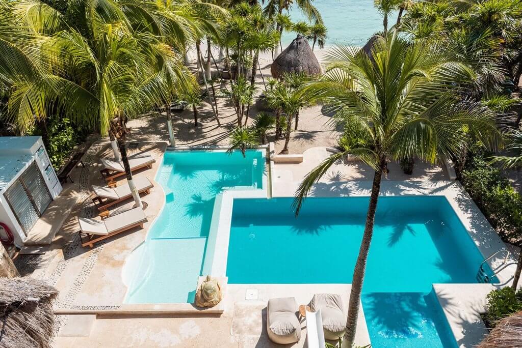 Sombras del Viento in Tulum, one of the top 10 Christmas holiday destinations, with pools, palm trees, loungers, and beachfront views.