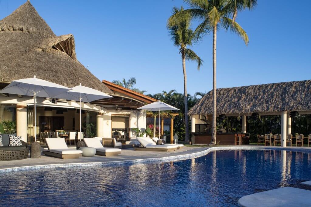 Casa del Faro with sunlit lounges, palms, and a tranquil pool by the sea.