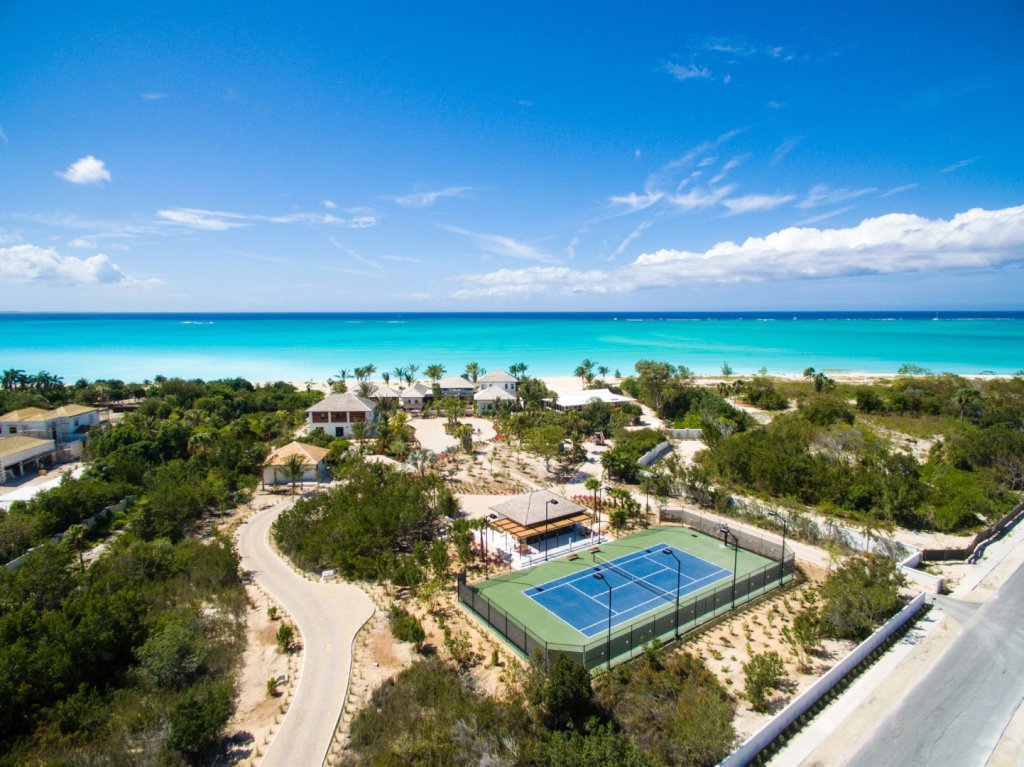 Aerial view of Villa Hawksbill on Turks & Caicos featuring beachfront villas, tennis court, and turquoise ocean.
