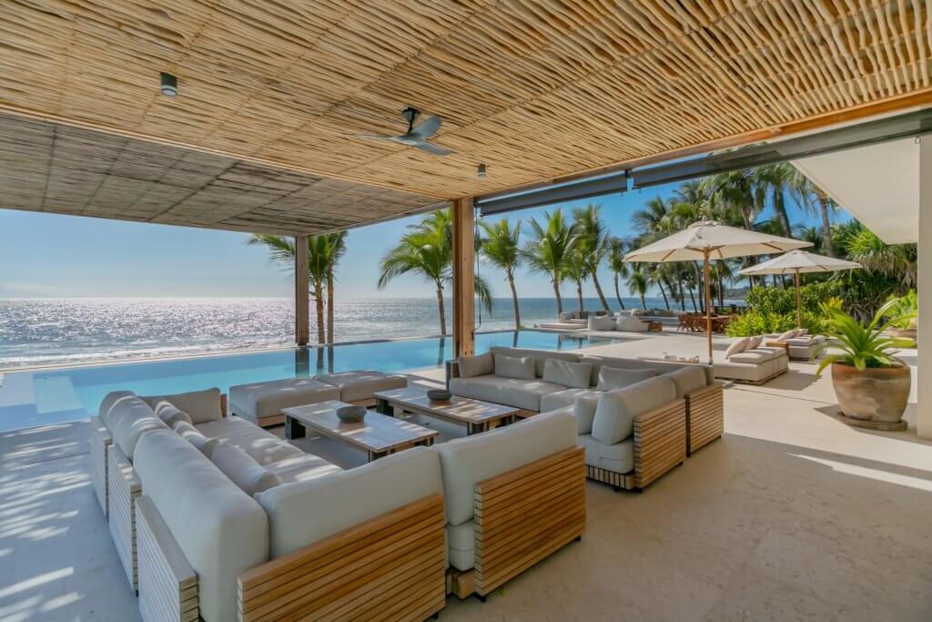 Villa living experiences at Casa Veneros with oceanfront lounge, shaded seating, infinity pool, and palm-lined views over Punta Mita’s coast.