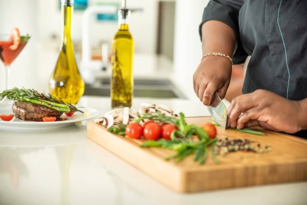 Luxury villa vacation with kids at Amalia, St Martin, private chef slicing herbs beside gourmet steak and fresh produce.
