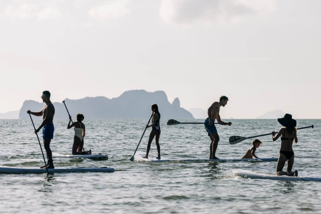 Guests at Àni Villa Thailand enjoy guided paddleboarding on calm waters framed by distant limestone islands.