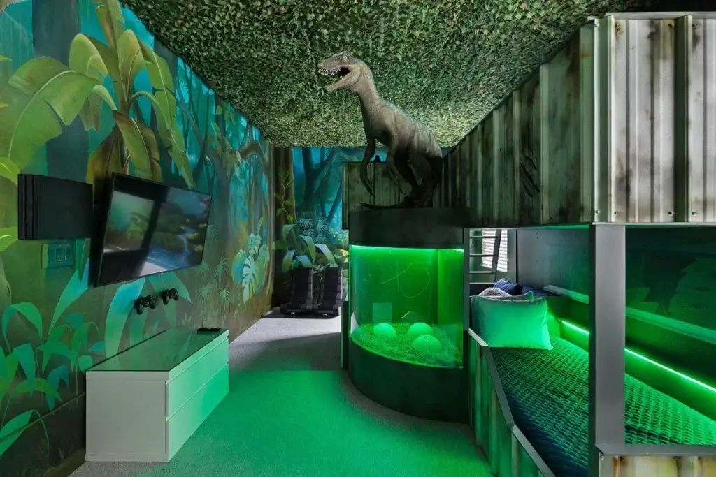 Immersive jungle bunk room with neon lighting, gaming setup, and a life-sized dinosaur centerpiece