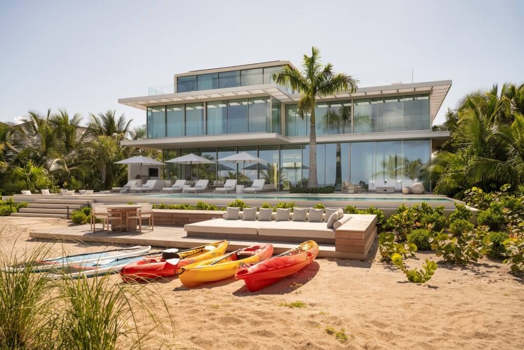 BE The Reserve Villa 1 with a beachfront pool, modern glass façade, and kayaks on Grace Bay